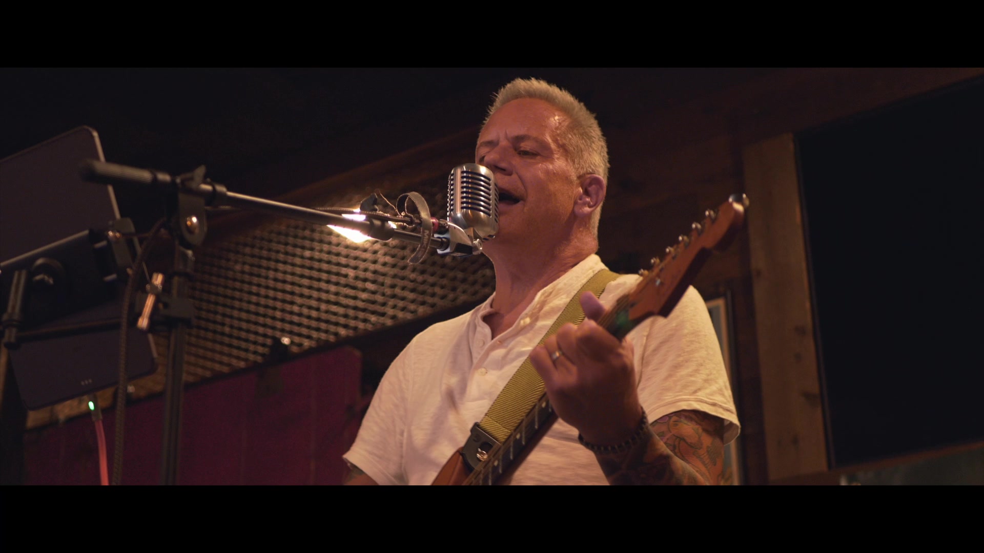 Close up of Mike Bush singing into a vintage microphone with guitar